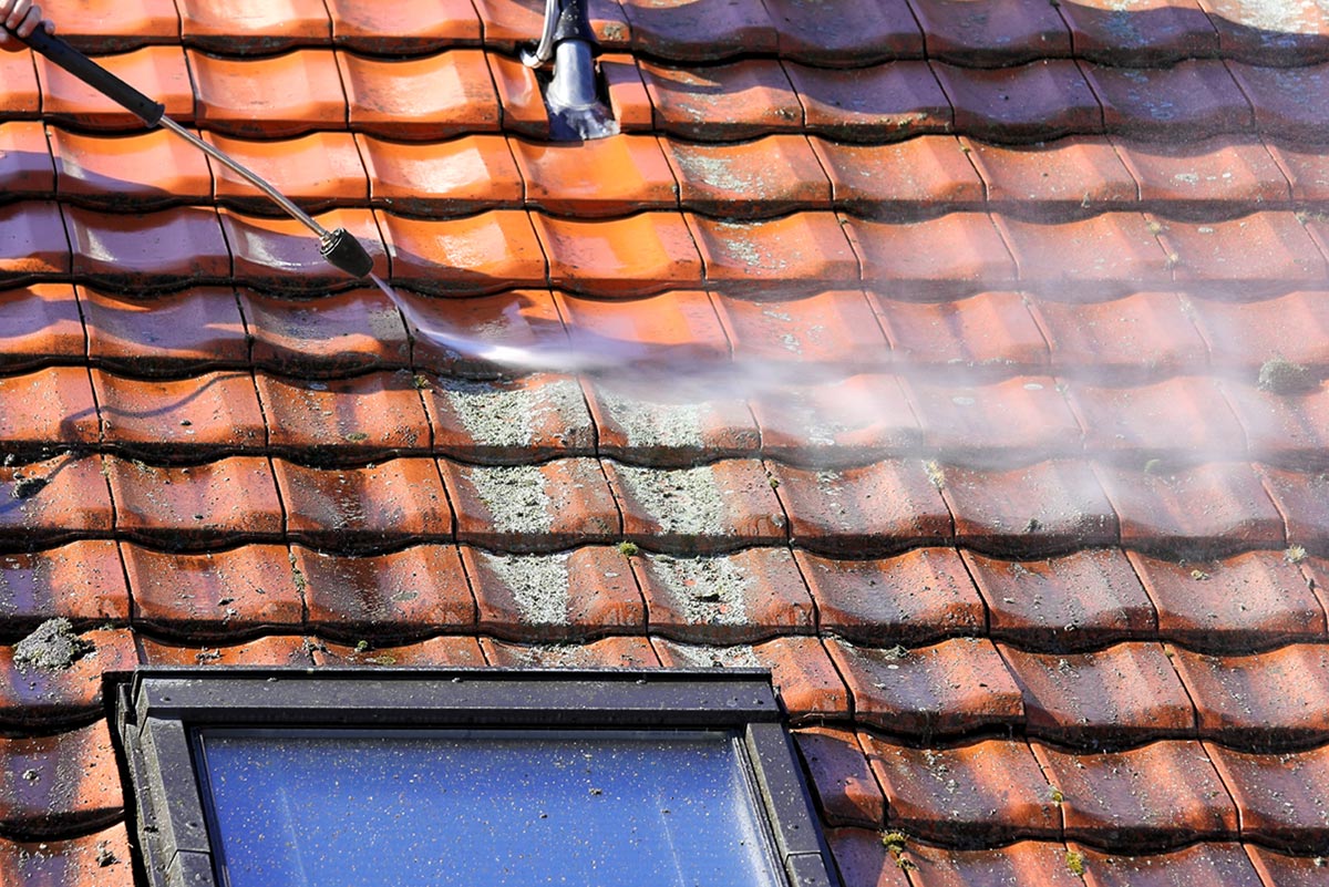 Lichen and grime being pressure cleaned from a terracotta tiled roof.
