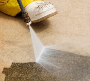 a man high pressure cleaning grime and mildew off a concrete surface